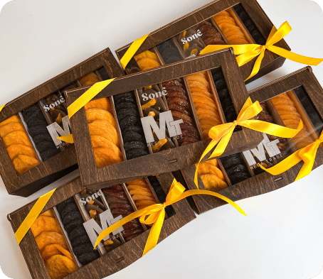 Wooden gift boxes tied with yellow ribbon, filled with dried apricots, plums, and raisins under a custom client logo