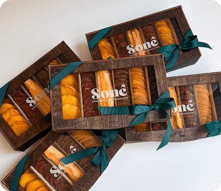 Sone gift boxes tied with teal ribbon, filled with rows of dried apricots, plums, and raisins